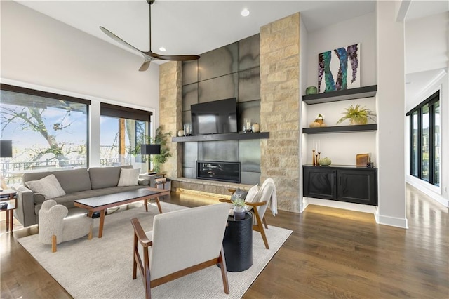 living room with dark wood-type flooring, a large fireplace, a healthy amount of sunlight, and a towering ceiling