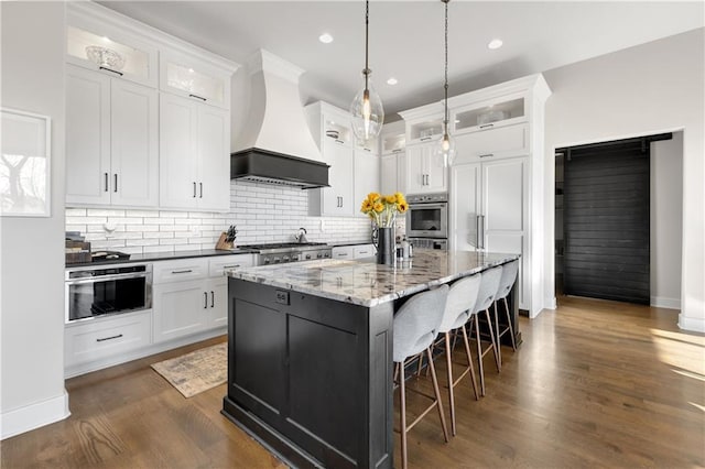 kitchen with white cabinetry, hanging light fixtures, a kitchen island with sink, and custom exhaust hood