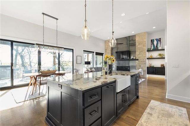 kitchen featuring wood-type flooring, sink, hanging light fixtures, light stone counters, and a center island with sink