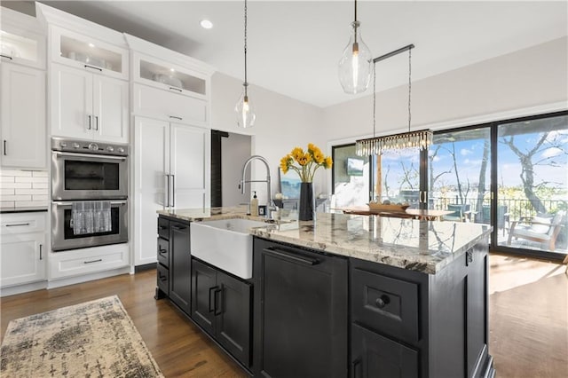 kitchen featuring sink, hanging light fixtures, a center island with sink, stainless steel double oven, and white cabinets