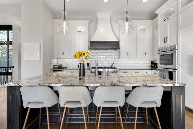 kitchen with premium range hood, a spacious island, double oven, and white cabinets