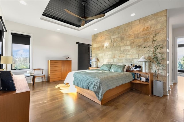 bedroom with hardwood / wood-style floors, a tray ceiling, wooden ceiling, and a barn door