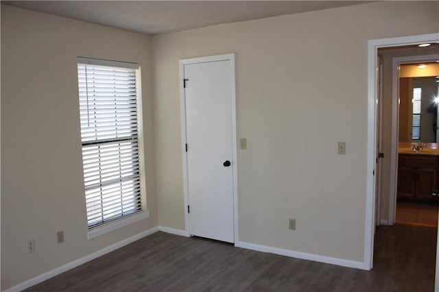 unfurnished bedroom featuring dark hardwood / wood-style floors, sink, and ensuite bath