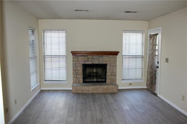 unfurnished living room with dark hardwood / wood-style floors, a textured ceiling, a stone fireplace, and a wealth of natural light