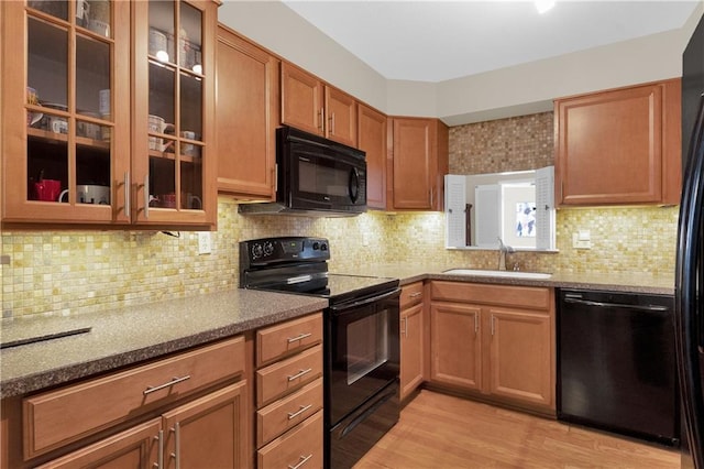 kitchen featuring sink, dark stone counters, decorative backsplash, light hardwood / wood-style floors, and black appliances