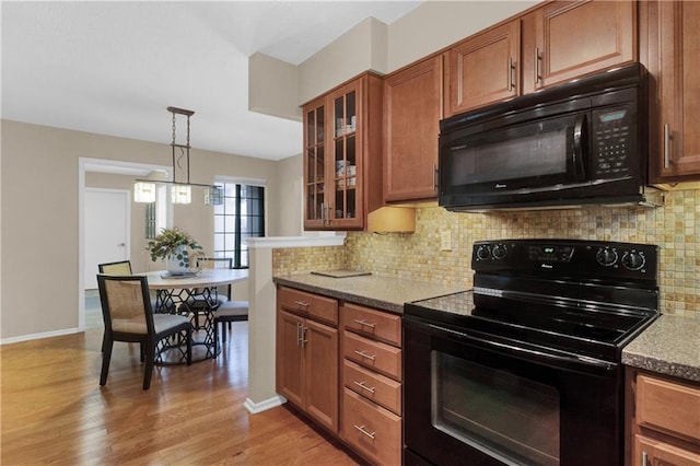 kitchen with light stone counters, pendant lighting, black appliances, and light hardwood / wood-style floors