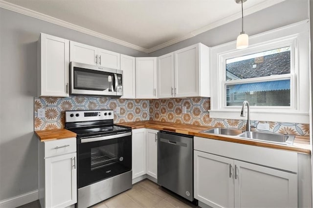 kitchen with appliances with stainless steel finishes, decorative light fixtures, white cabinetry, sink, and butcher block counters