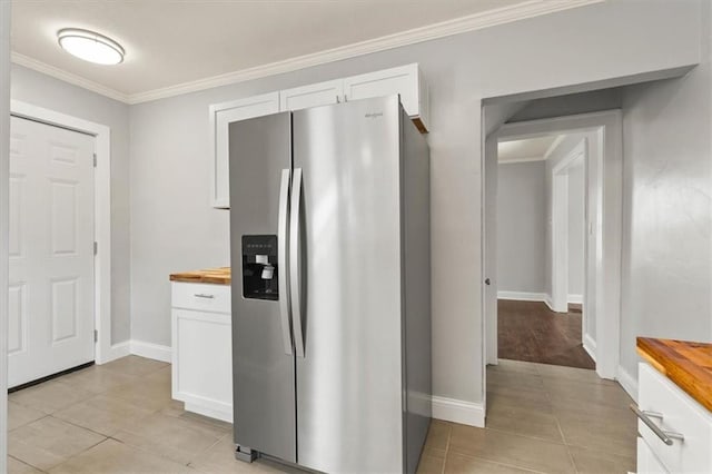 kitchen featuring crown molding, stainless steel fridge, white cabinets, light tile patterned flooring, and wood counters