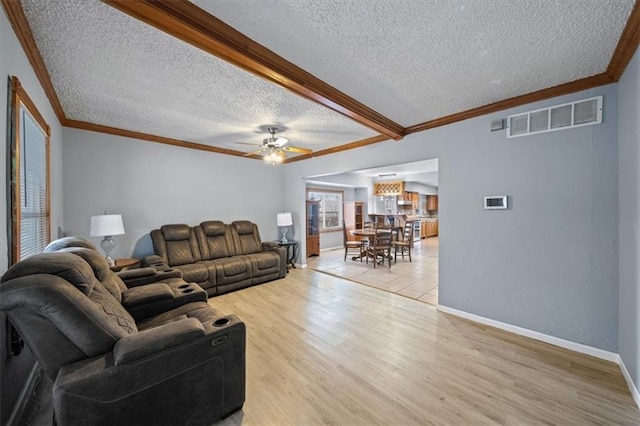 living room featuring crown molding, visible vents, light wood-style flooring, a textured ceiling, and baseboards