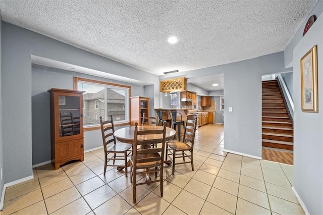 dining room featuring light tile patterned flooring, a textured ceiling, baseboards, and stairs