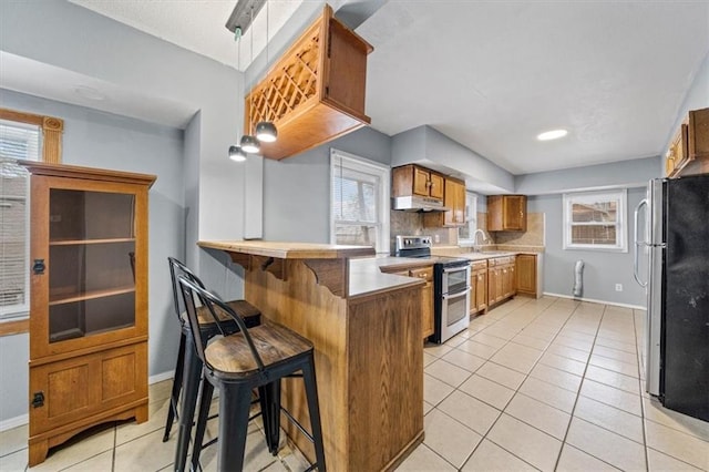 kitchen featuring stainless steel appliances, light tile patterned flooring, under cabinet range hood, and a peninsula