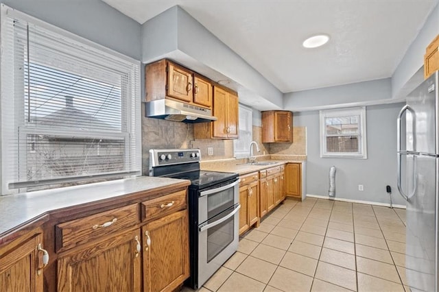 kitchen with light tile patterned floors, stainless steel appliances, tasteful backsplash, a sink, and under cabinet range hood