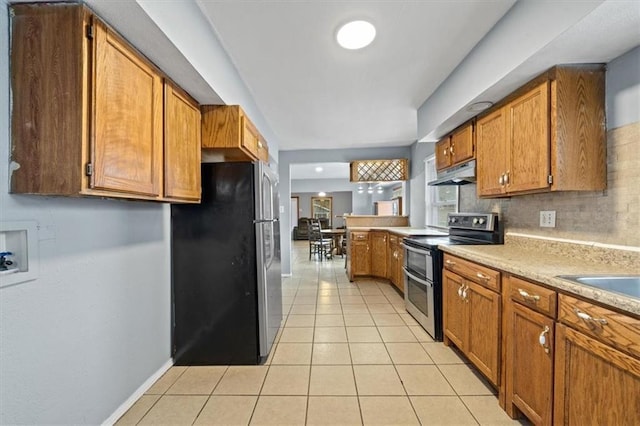 kitchen with light tile patterned floors, stainless steel appliances, brown cabinetry, and under cabinet range hood