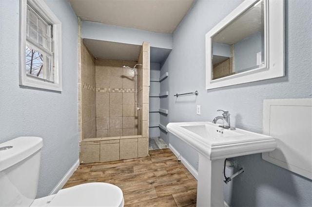 bathroom with tiled shower, toilet, and wood finished floors