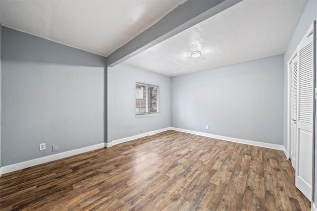 unfurnished bedroom featuring a closet, baseboards, wood finished floors, and beamed ceiling