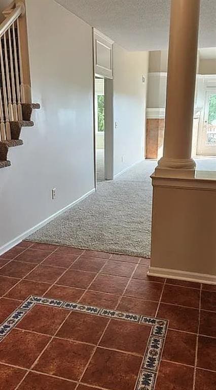 carpeted spare room featuring decorative columns and a textured ceiling