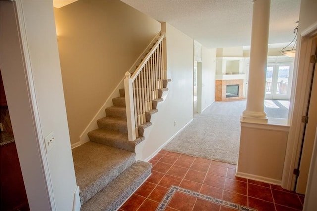 stairs with a fireplace, carpet floors, and decorative columns