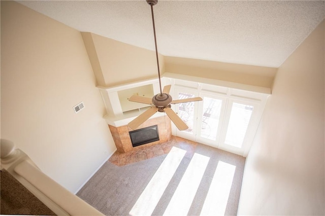 unfurnished living room featuring ceiling fan, a fireplace, a textured ceiling, light carpet, and vaulted ceiling