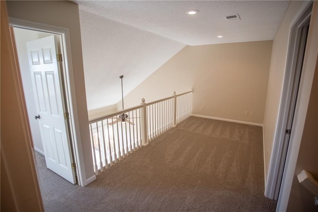 hallway with vaulted ceiling, a textured ceiling, and dark colored carpet