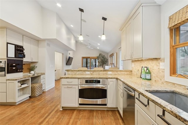 kitchen with decorative light fixtures, sink, kitchen peninsula, stainless steel appliances, and light hardwood / wood-style flooring