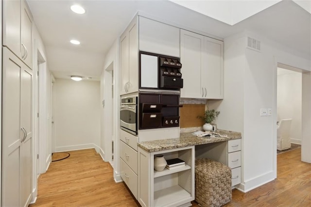 kitchen featuring white cabinetry, stainless steel oven, light stone counters, and light hardwood / wood-style floors