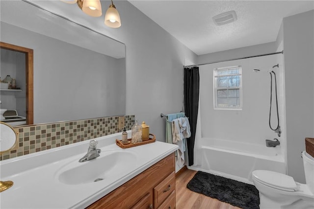 full bathroom with hardwood / wood-style flooring, vanity, shower / tub combo, toilet, and a textured ceiling