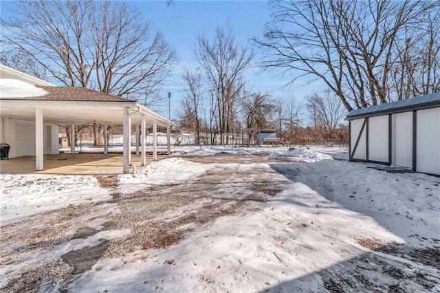 yard layered in snow featuring a carport and a storage shed