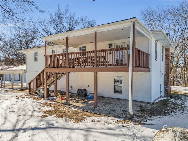 snow covered back of property with a wooden deck and central AC