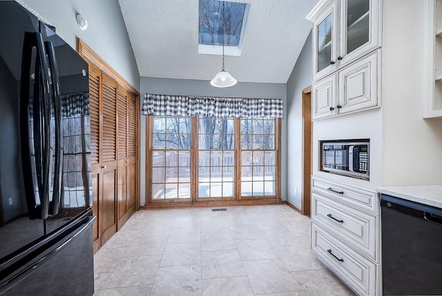 kitchen with lofted ceiling with skylight, white cabinetry, light stone counters, hanging light fixtures, and black appliances