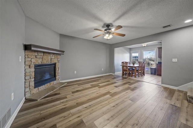 unfurnished living room featuring hardwood / wood-style floors, a stone fireplace, a textured ceiling, and ceiling fan