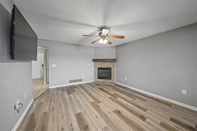 unfurnished living room featuring ceiling fan, a stone fireplace, light hardwood / wood-style floors, and a textured ceiling