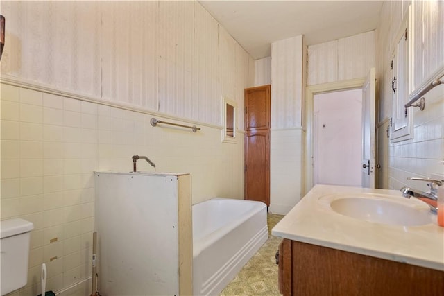 bathroom with tile walls, vanity, a tub, and toilet