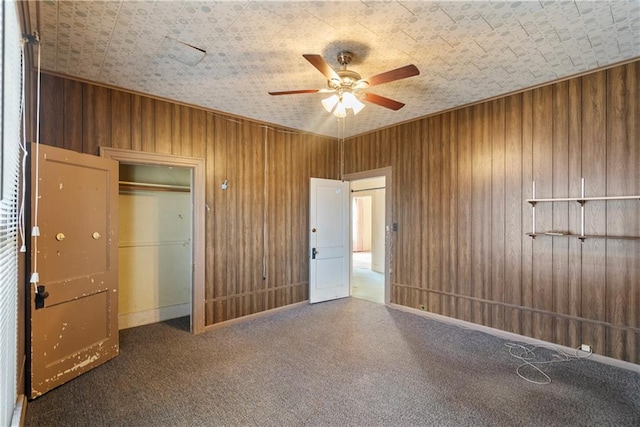 unfurnished bedroom featuring ceiling fan, wooden walls, dark carpet, and a closet