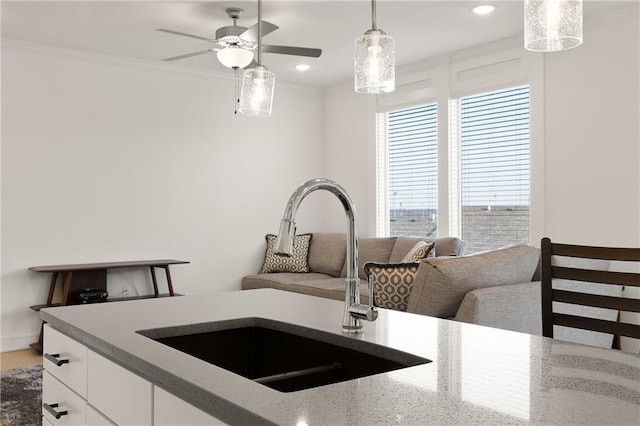 kitchen with sink, crown molding, light stone counters, white cabinets, and decorative light fixtures