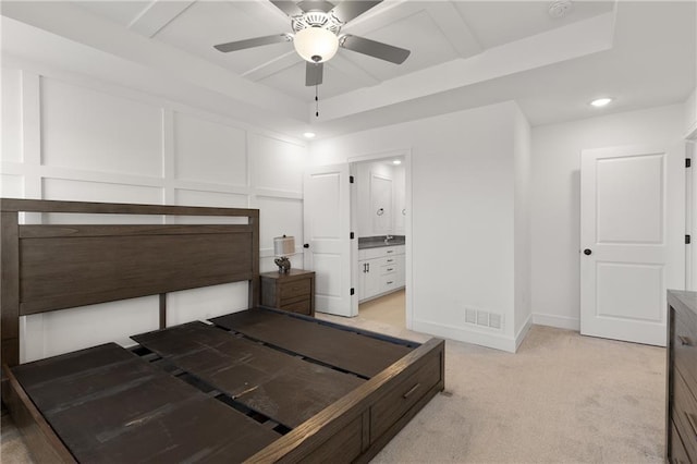 carpeted bedroom featuring ceiling fan, ensuite bath, and a raised ceiling