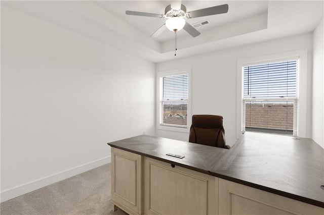 unfurnished office with ceiling fan, a raised ceiling, and light colored carpet