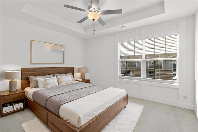 carpeted bedroom with ceiling fan and a tray ceiling