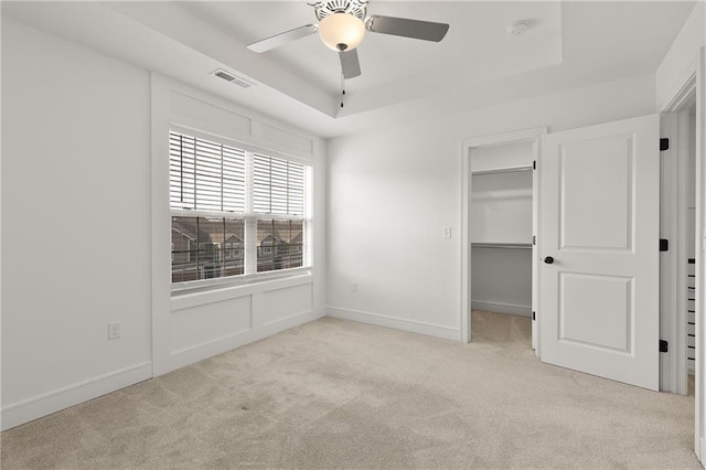 unfurnished bedroom featuring a tray ceiling, light carpet, and a spacious closet