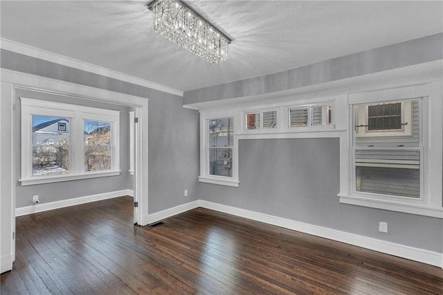 empty room with dark wood-type flooring, ornamental molding, and a notable chandelier