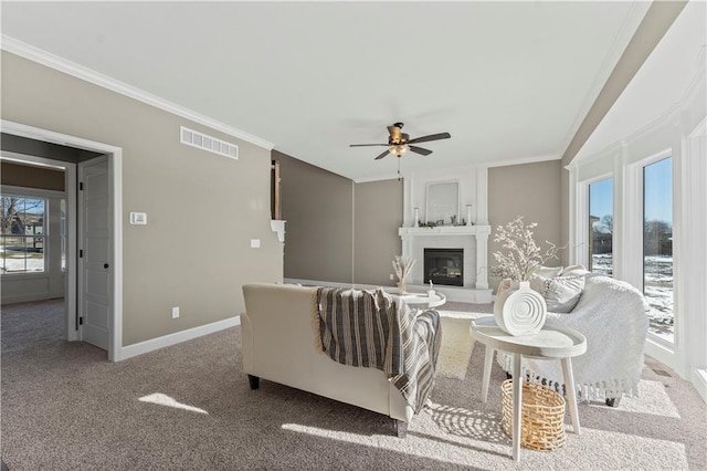 carpeted living room with ceiling fan, a large fireplace, plenty of natural light, and ornamental molding