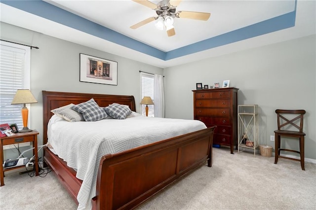 carpeted bedroom with a raised ceiling and ceiling fan