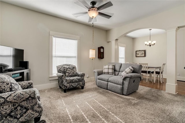 carpeted living room with ceiling fan with notable chandelier, plenty of natural light, and ornate columns