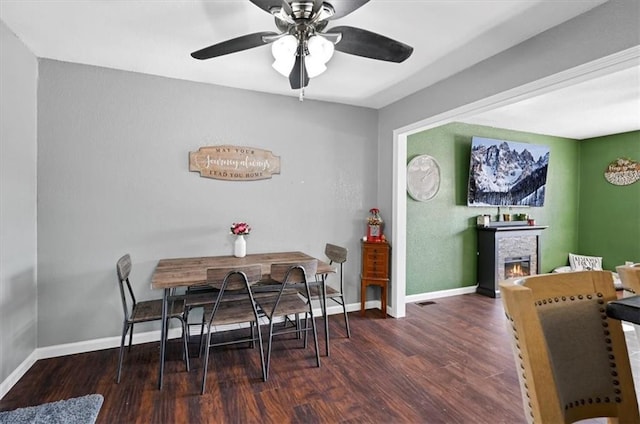 dining space with a stone fireplace, dark hardwood / wood-style floors, and ceiling fan