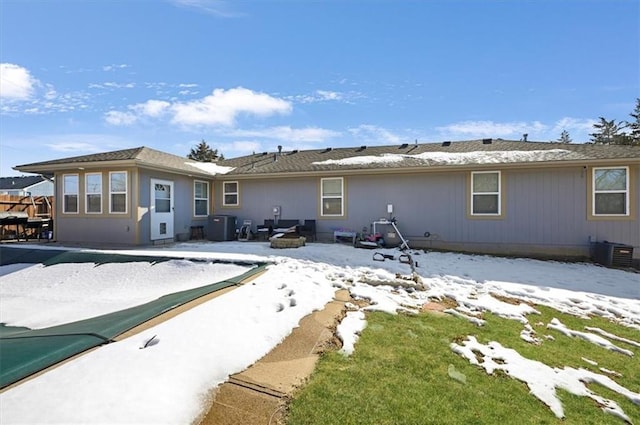 snow covered rear of property featuring cooling unit, a fire pit, and a patio