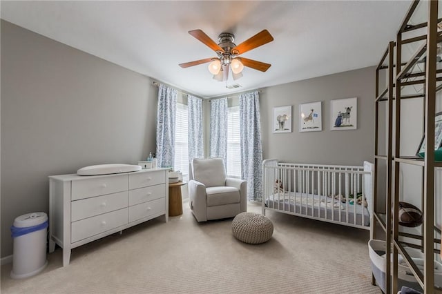 carpeted bedroom featuring a crib and ceiling fan