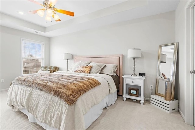 bedroom with ceiling fan, a tray ceiling, and light carpet