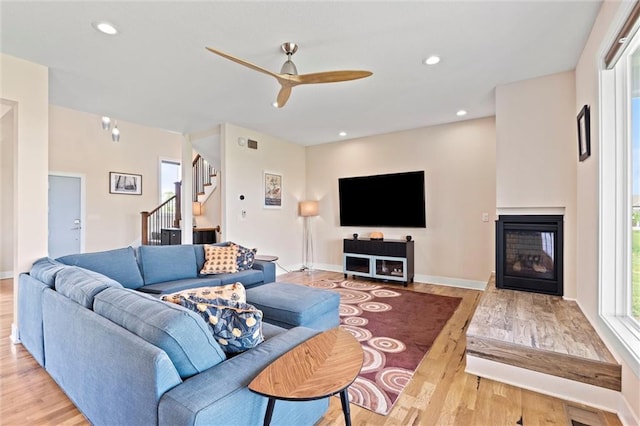 living area featuring a multi sided fireplace, a ceiling fan, light wood finished floors, and stairway