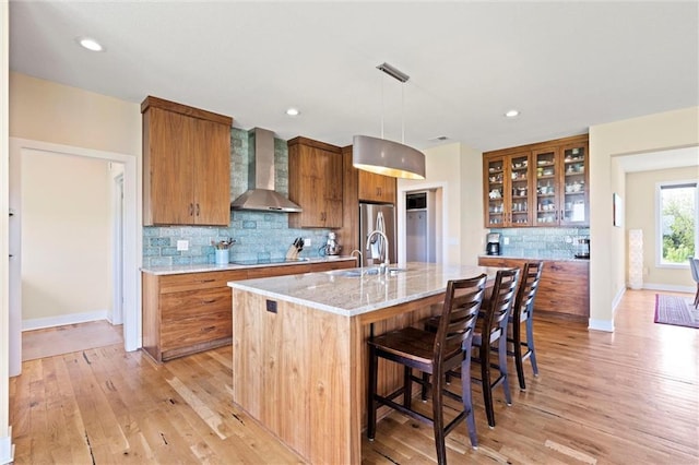 kitchen with a kitchen breakfast bar, brown cabinetry, tasteful backsplash, light wood-type flooring, and wall chimney exhaust hood