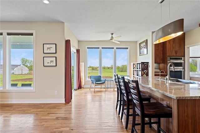 kitchen with a breakfast bar area, light wood-type flooring, a sink, light stone counters, and double oven