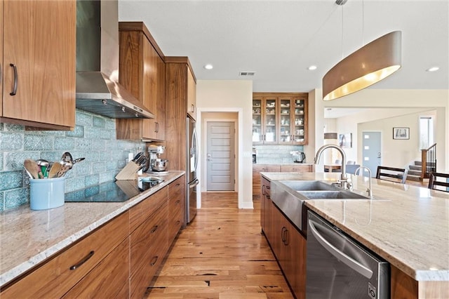kitchen featuring a large island, wall chimney exhaust hood, brown cabinets, a sink, and appliances with stainless steel finishes